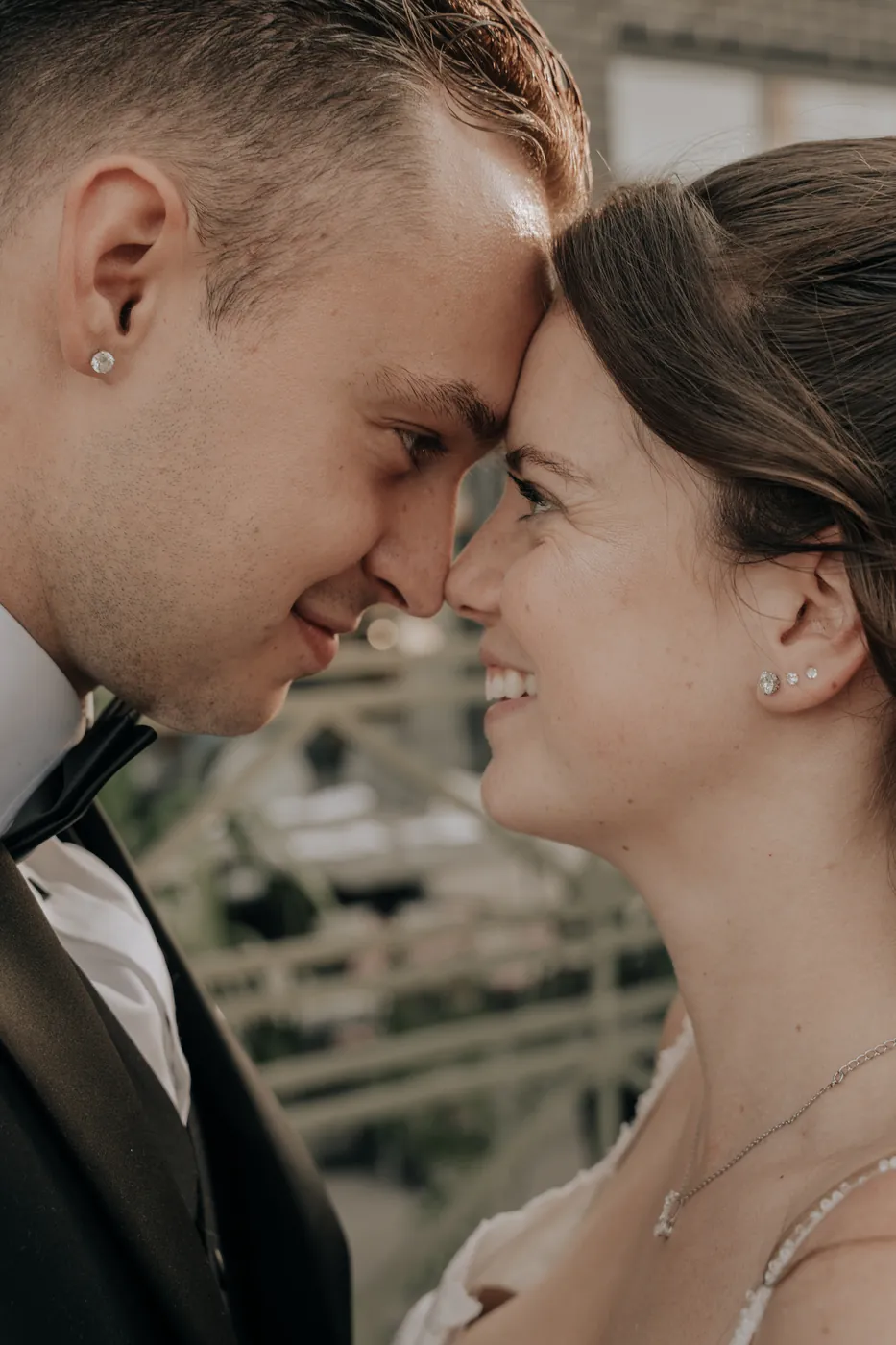 A bride and groom face to face, foreheads almost touching, smiling.